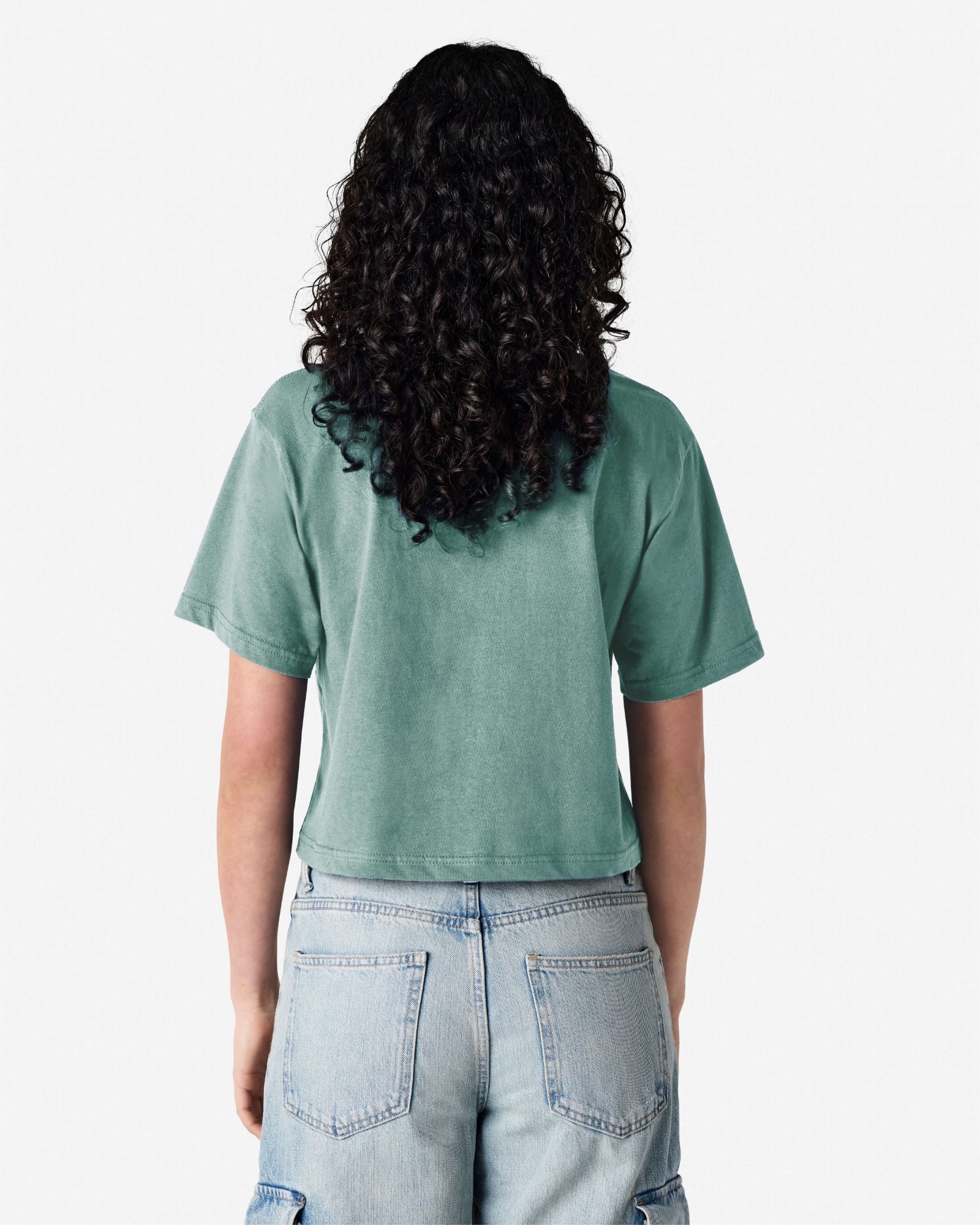 Female model wearing an American Apparel Fine Jersey Women's Boxy Tee in arctic, paired with blue jeans, standing against a plain background (back pose) -arctic