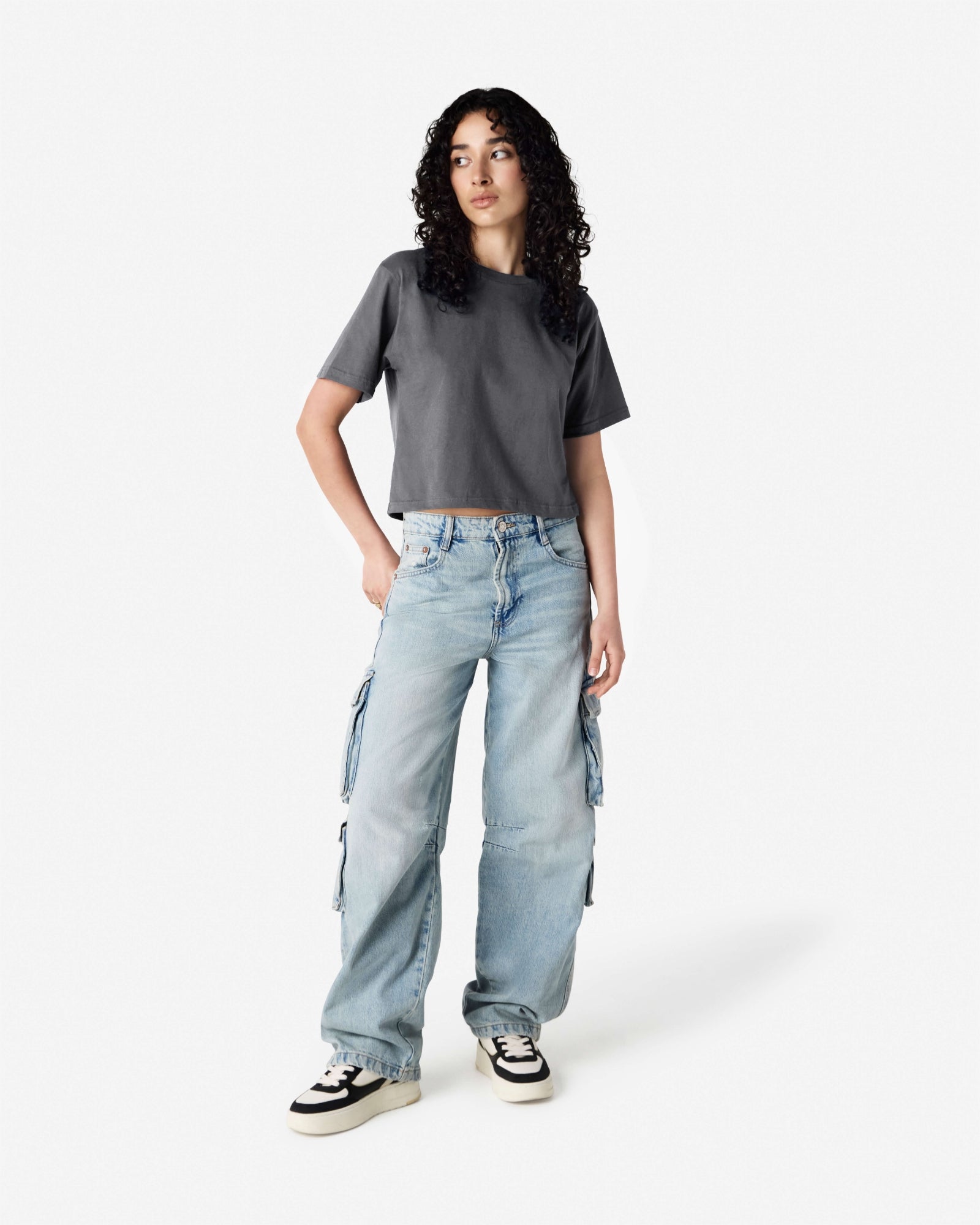 Female model wearing an American Apparel Fine Jersey Women's Boxy Tee in Asphalt, paired with blue jeans, standing against a plain background (front pose) -asphalt