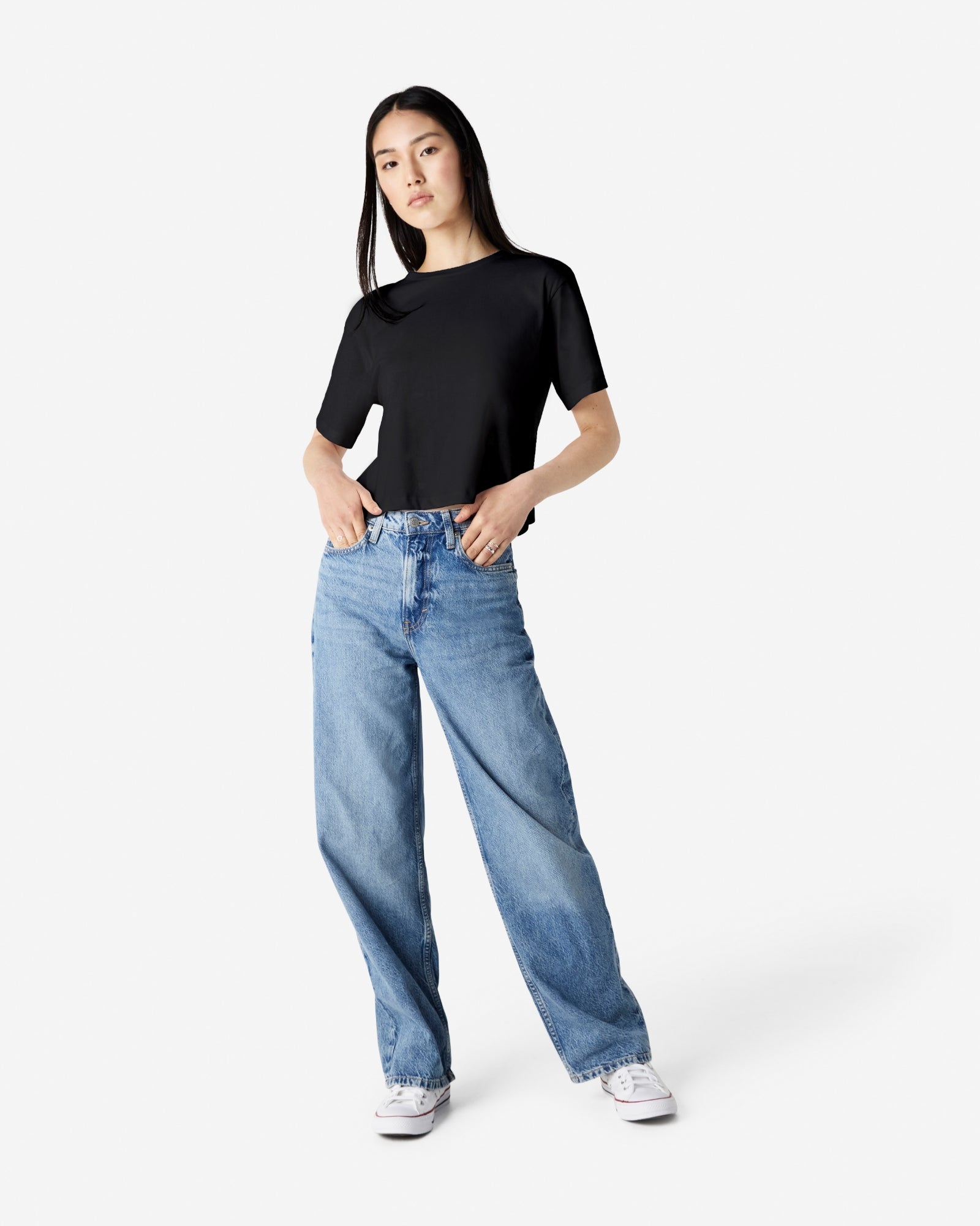 Female model wearing an American Apparel Fine Jersey Women's Boxy Tee in Black, paired with blue jeans, standing against a plain background (front pose) -black