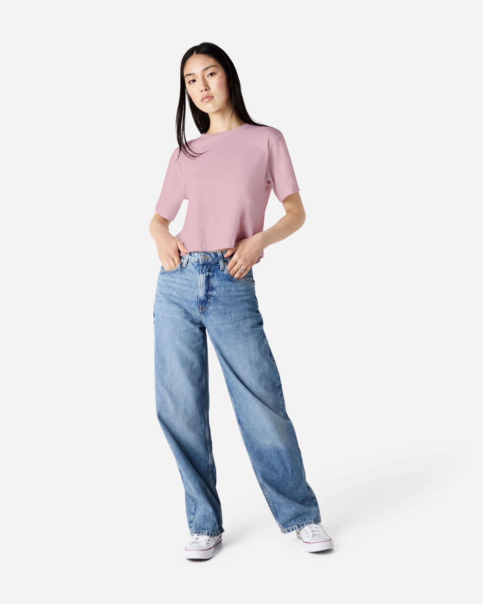 Female model wearing an American Apparel Fine Jersey Women's Boxy Tee in Blush, paired with blue jeans, standing against a plain background (front pose) -blush