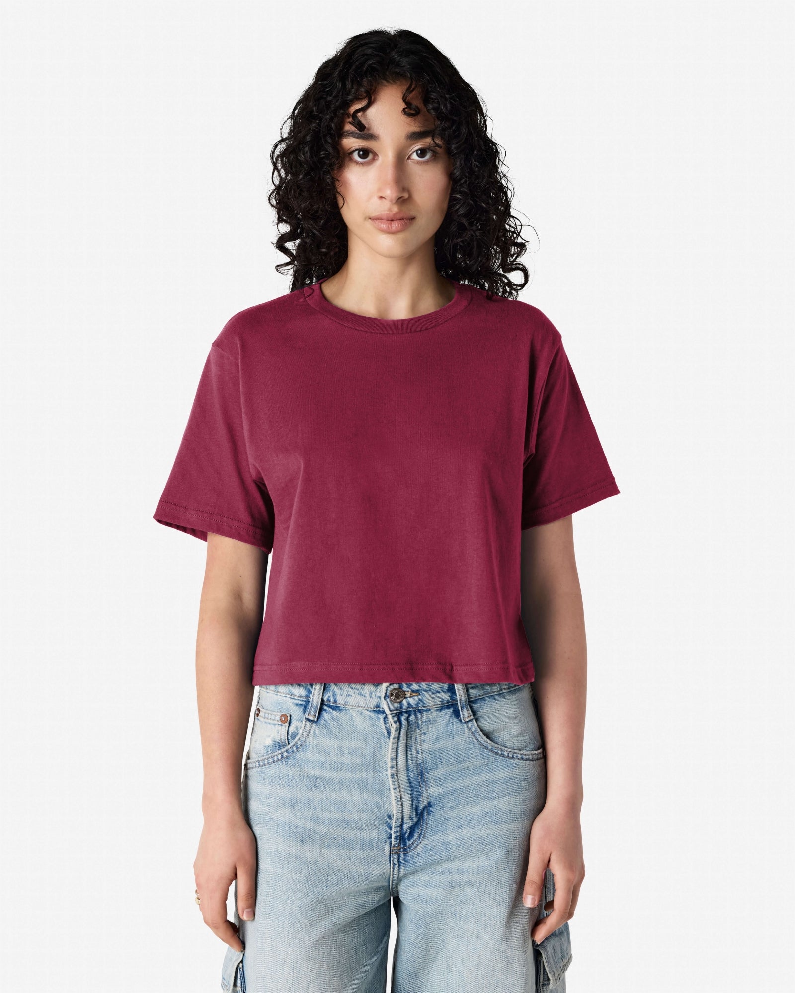 Female model wearing an American Apparel Fine Jersey Women's Boxy Tee in Burgundy, paired with blue jeans, standing against a plain background (front pose) -burgundy