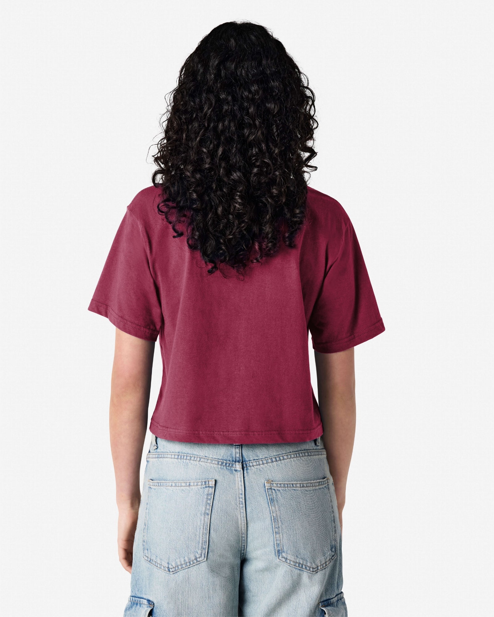 Female model wearing an American Apparel Fine Jersey Women's Boxy Tee in Burgundy, paired with blue jeans, standing against a plain background (back pose) -burgundy