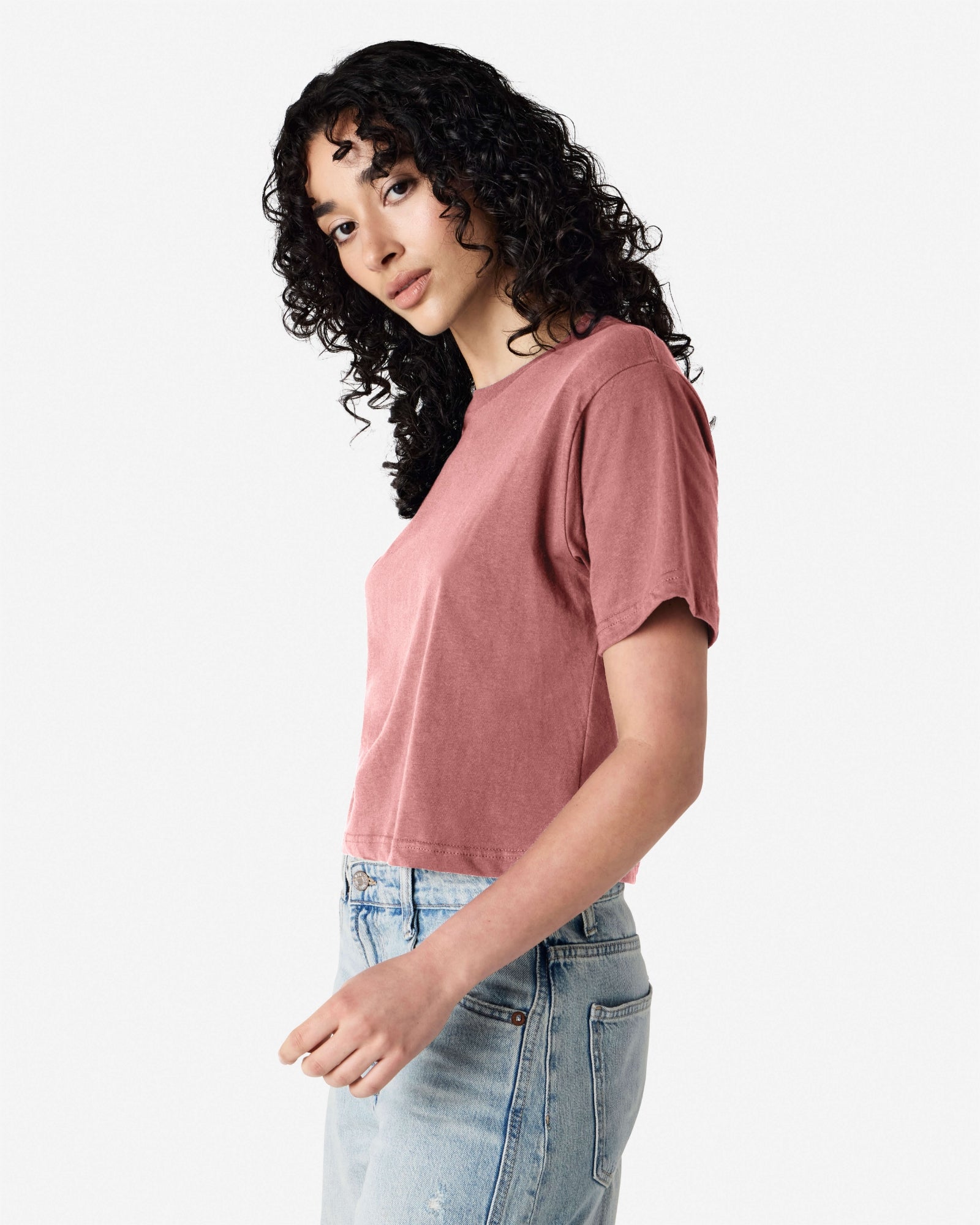 Female model wearing an American Apparel Fine Jersey Women's Boxy Tee in Canyon, paired with blue jeans, standing against a plain background (side pose) -canyon