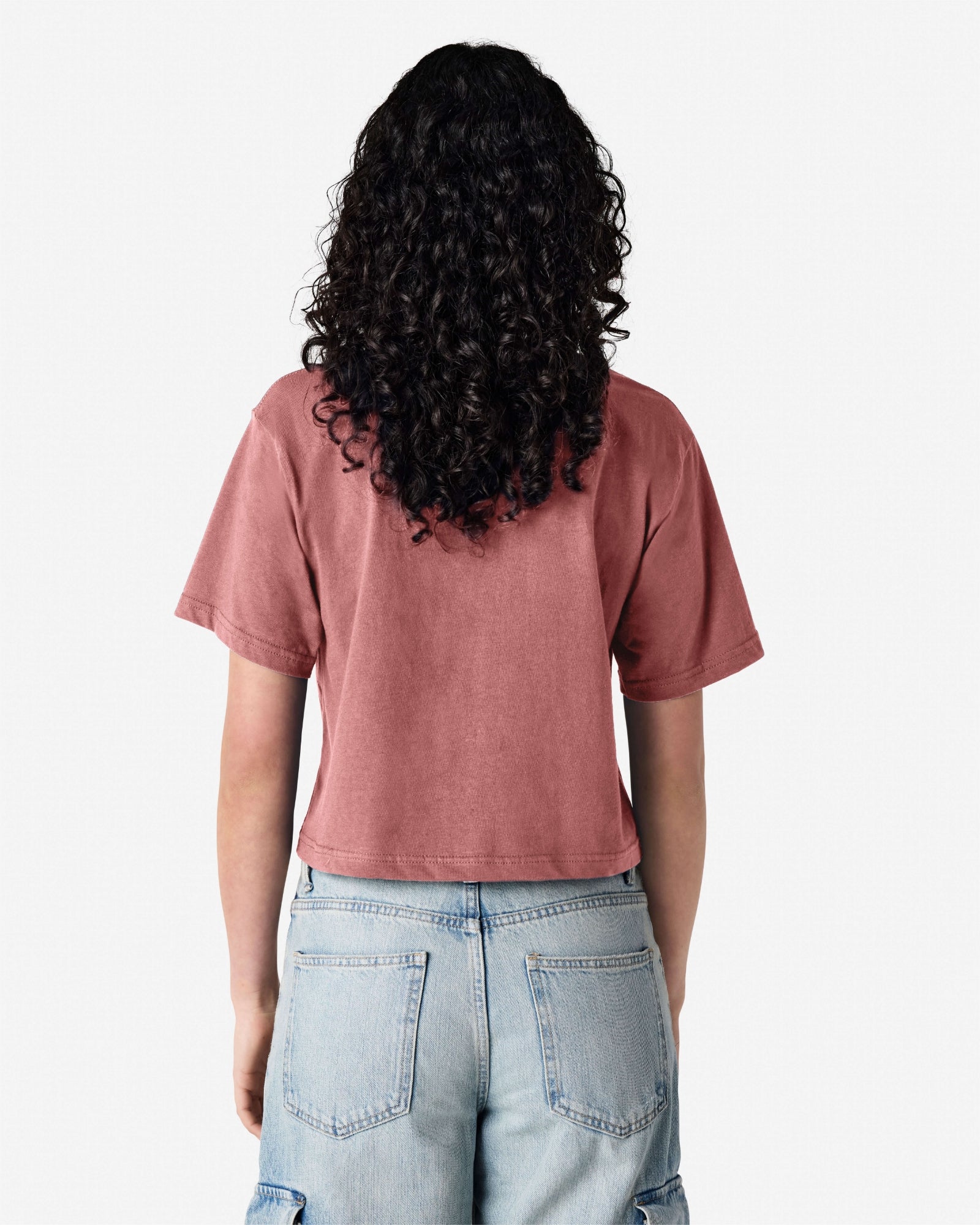 Female model wearing an American Apparel Fine Jersey Women's Boxy Tee in Canyon, paired with blue jeans, standing against a plain background (back pose) -canyon