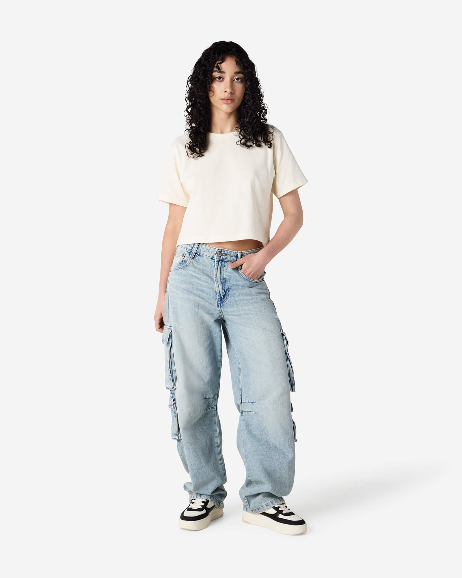 Female model wearing an American Apparel Fine Jersey Women's Boxy Tee in Cream, paired with blue jeans, standing against a plain background (front pose) -cream