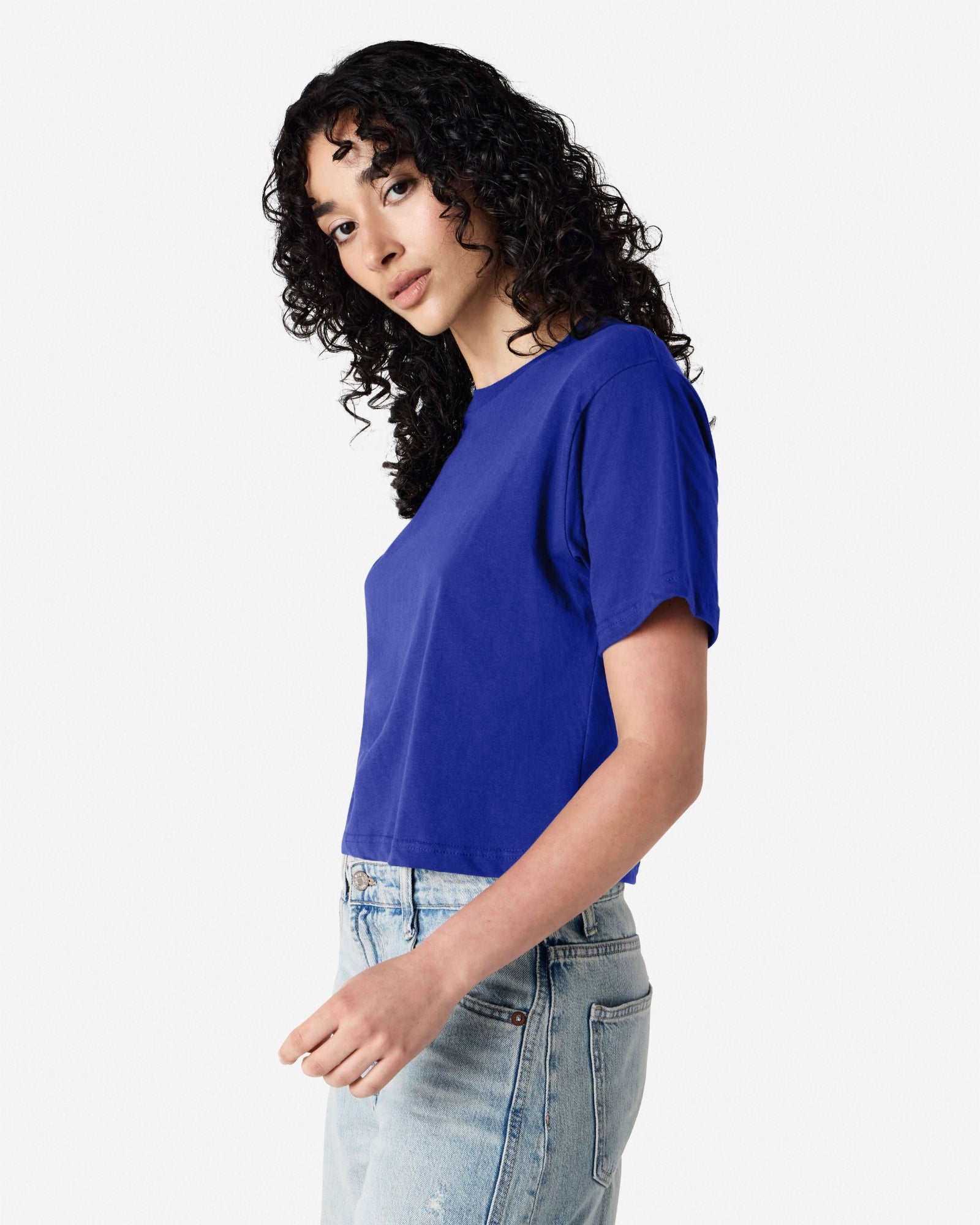 Female model wearing an American Apparel Fine Jersey Women's Boxy Tee in Lapis, paired with blue jeans, standing against a plain background (side pose) -lapis