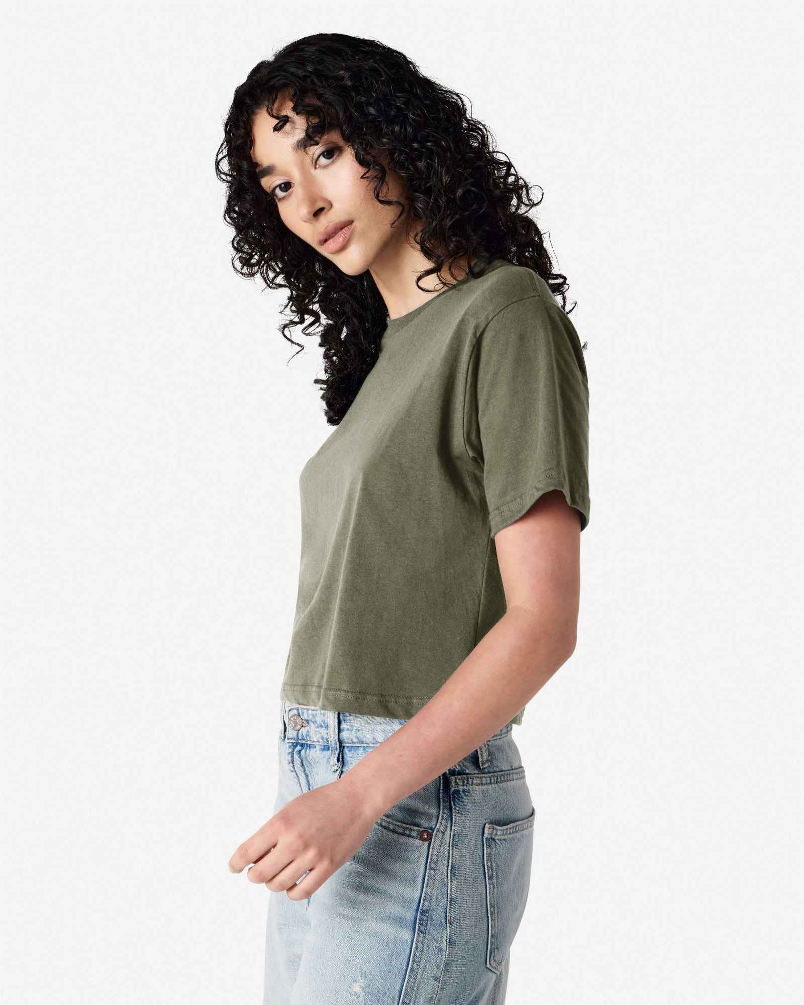 Female model wearing an American Apparel Fine Jersey Women's Boxy Tee in Liuetenant, paired with blue jeans, standing against a plain background (side pose) -liuetenant