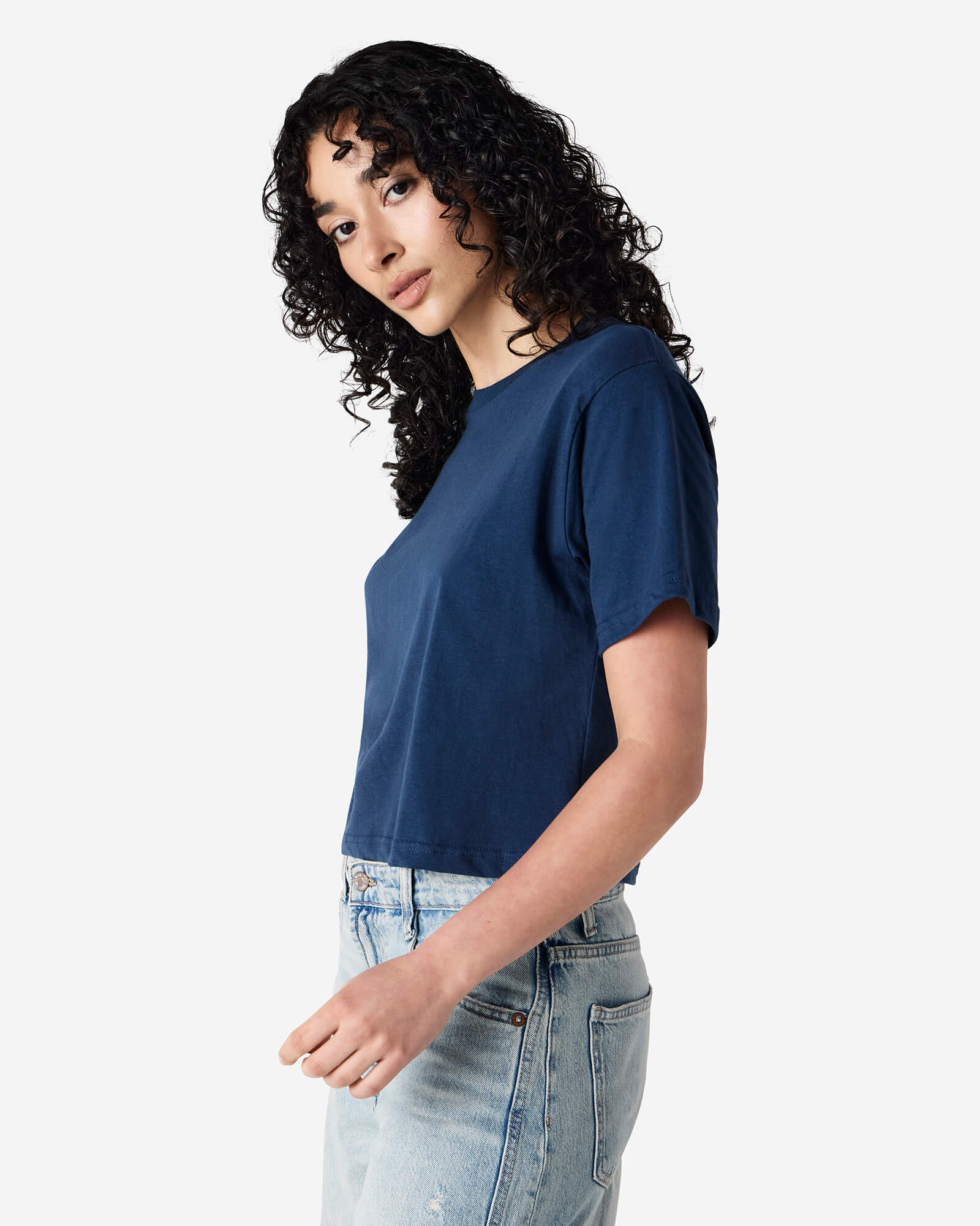 Female model wearing an American Apparel Fine Jersey Women's Boxy Tee in Sea Blue, paired with blue jeans, standing against a plain background (side pose) -sea blue