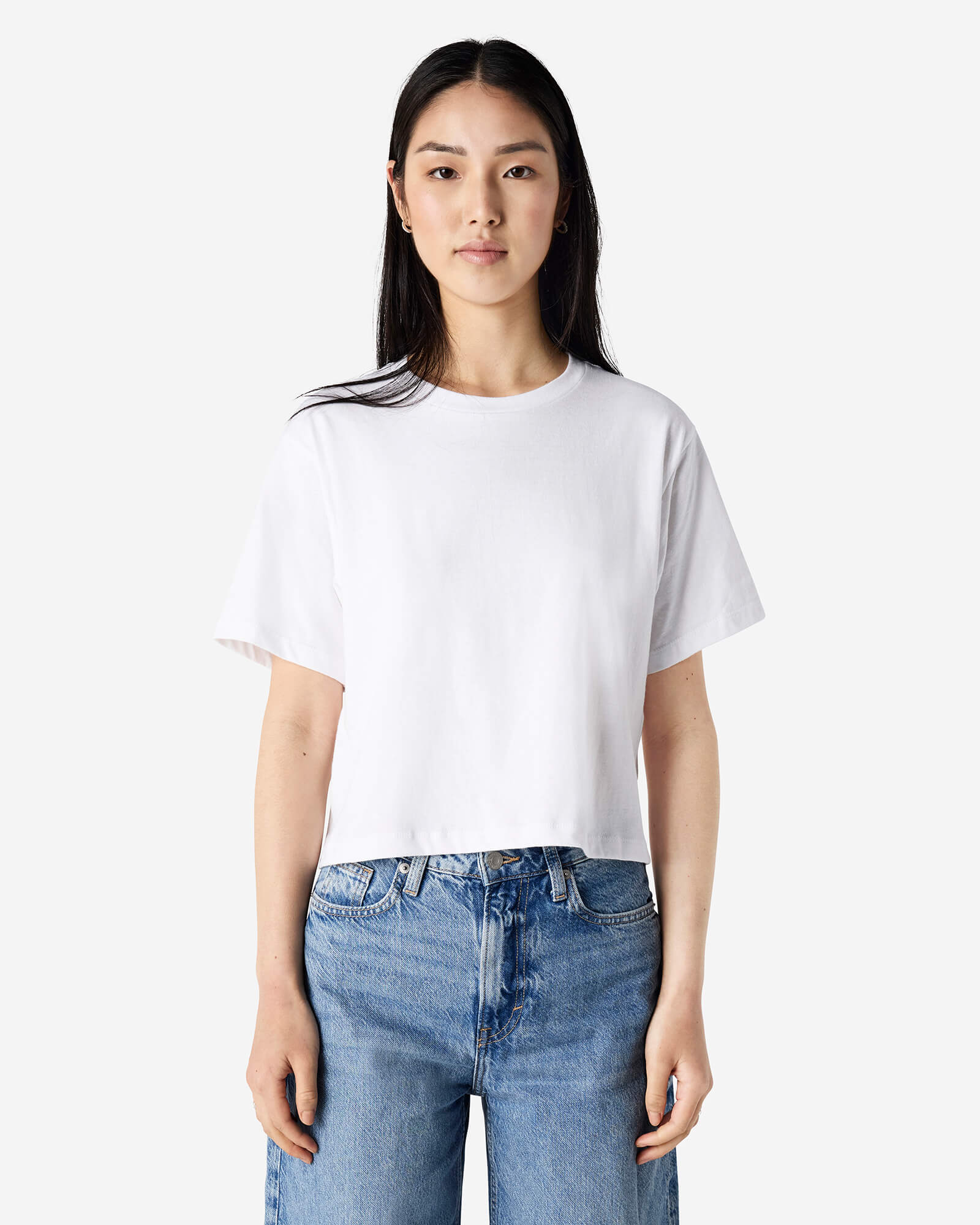 Female model wearing an American Apparel Fine Jersey Women's Boxy Tee in White, paired with blue jeans, standing against a plain background (front pose) -white