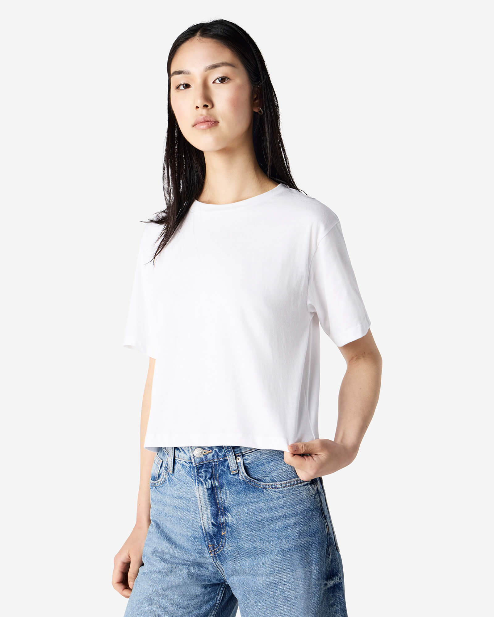 Female model wearing an American Apparel Fine Jersey Women's Boxy Tee in White, paired with blue jeans, standing against a plain background (front pose) -white