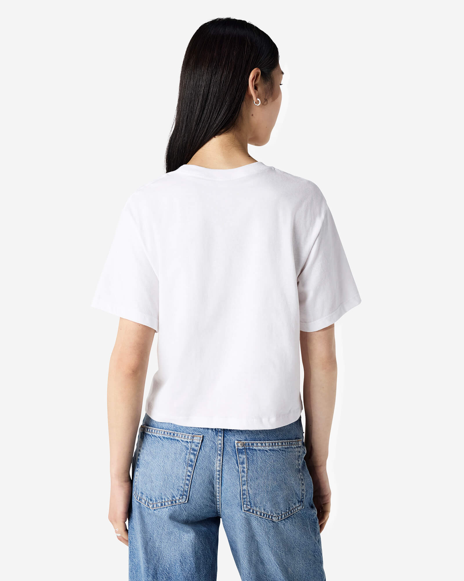 Female model wearing an American Apparel Fine Jersey Women's Boxy Tee in White, paired with blue jeans, standing against a plain background (back pose) -white