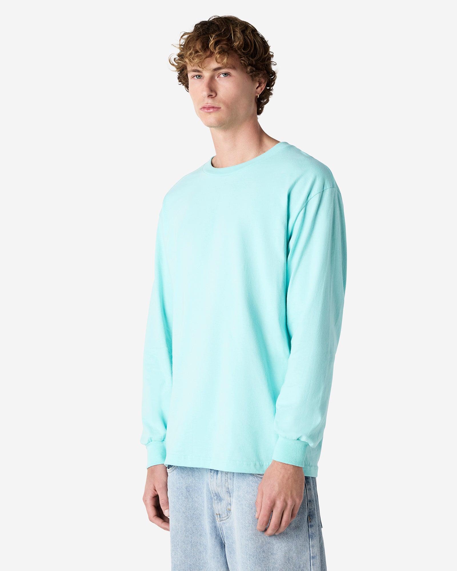 front view of a male Model wearing a Celadon colored Heavyweight Unisex Long Sleeve Crew Neck Tee, paired with blue jeans, standing against a plain background (front pose) -celadon