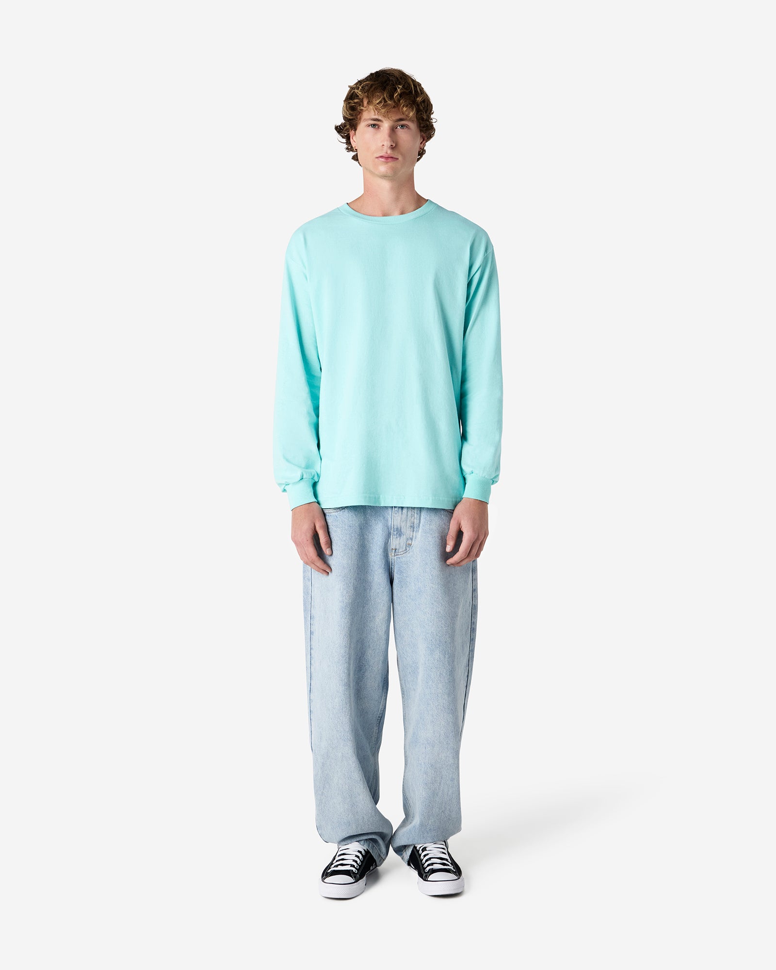 front view of a male Model wearing a Celadon colored Heavyweight Unisex Long Sleeve Crew Neck Tee, paired with blue jeans, standing against a plain background (front pose) -celadon