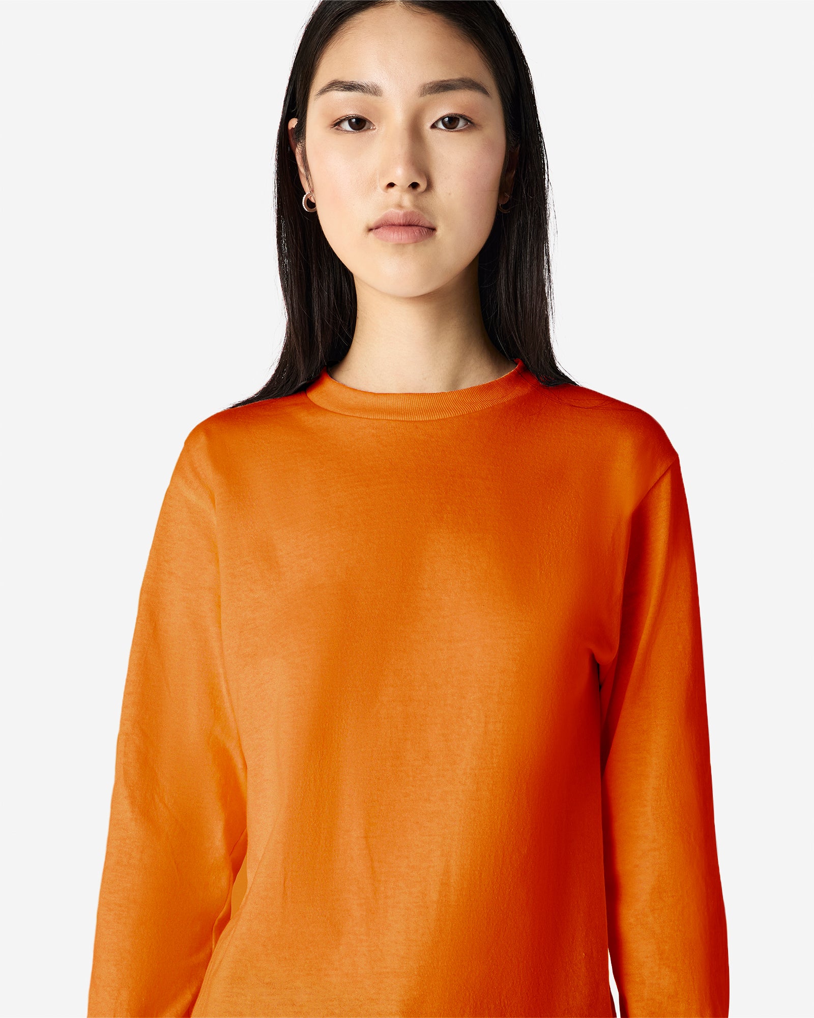 front view of a female Model wearing a Heather Orange Heavyweight Unisex Long Sleeve Crew Neck Tee, paired with blue jeans, standing against a plain background (front pose) -orange