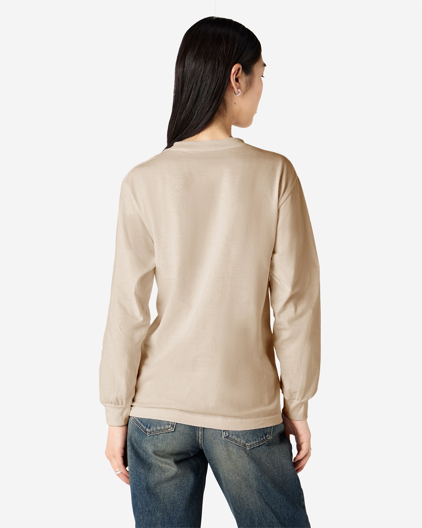 front view of a female Model wearing a Sand colored Heavyweight Unisex Long Sleeve Crew Neck Tee, paired with blue jeans, standing against a plain background (back pose) -sand