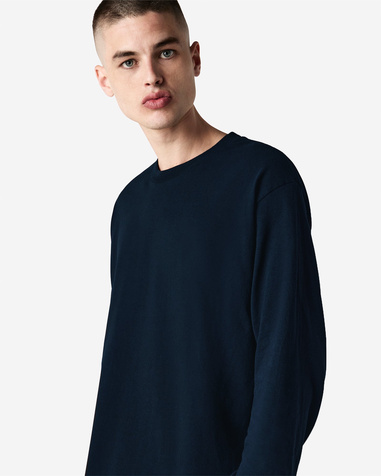 front view of a male Model wearing a True Navy colored Heavyweight Unisex Long Sleeve Crew Neck Tee, paired with blue jeans, standing against a plain background (front pose) -true navy