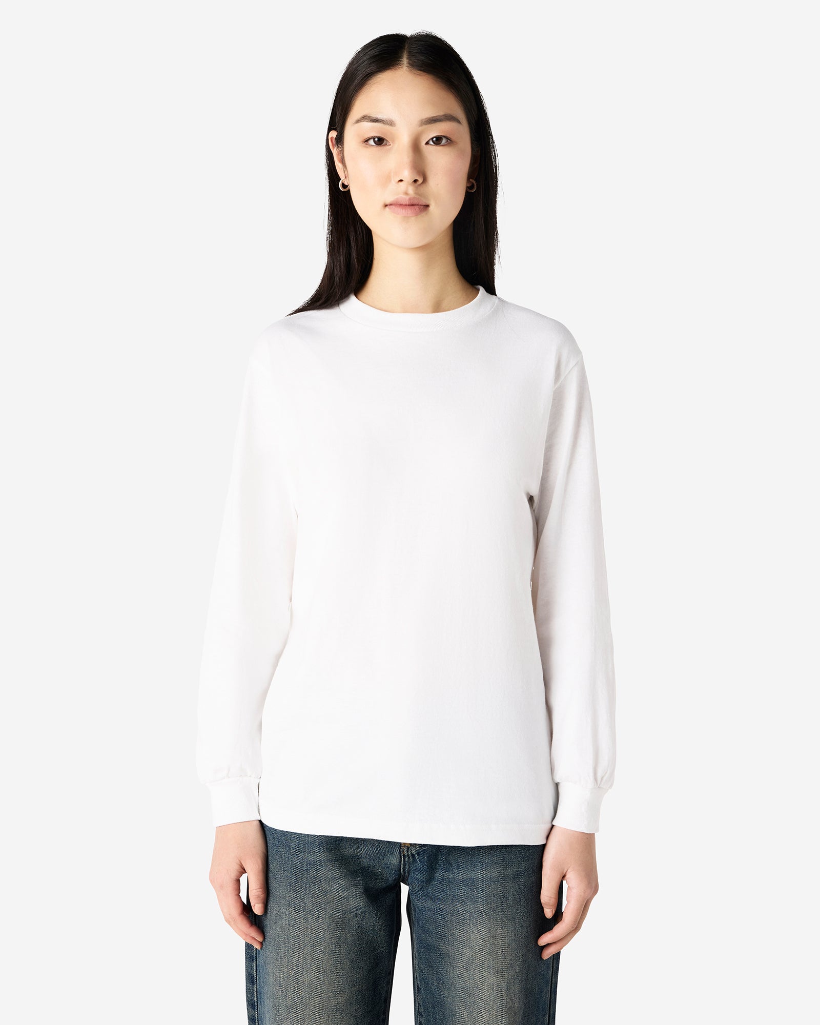 front view of a female Model wearing a White colored Heavyweight Unisex Long Sleeve Crew Neck Tee, paired with blue jeans, standing against a plain background (front pose) -white